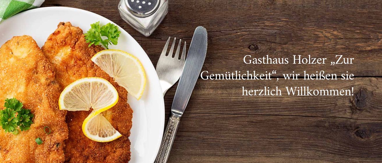 Ein weißer Teller mit gebratenem Fleisch, Petersilie und Zitronenscheiben, mit Gabel und Messer in der Nähe. Ein Salzstreuer steht auf dem Tisch. Das Wort Gemütlich ist darunter geschrieben.