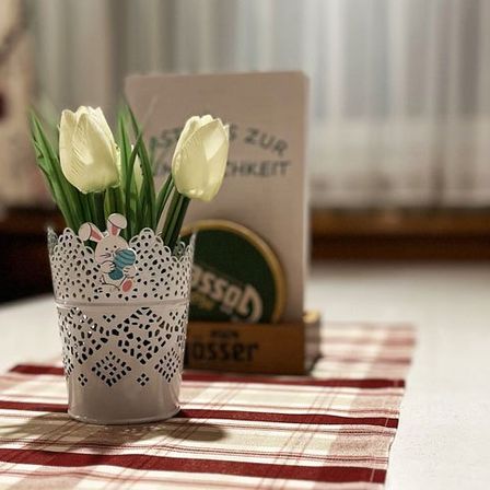 Ein Bouquet aus weißen Tulpen in einem dekorativen Glas auf einem Tisch mit rot-weiß kariertem Tuch.
