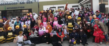 Eine Gruppe von Menschen in verschiedenen Kostümen, darunter Tiere, Insekten und Menschen, posiert für ein Foto vor einem Gebäude mit der Aufschrift 'RF AM SEE'.