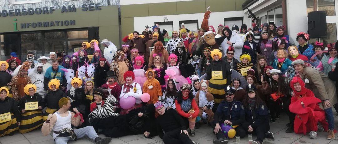 Eine Gruppe von Menschen in verschiedenen Kostümen, darunter Tiere, Insekten und Menschen, posiert für ein Foto vor einem Gebäude mit der Aufschrift 'RF AM SEE'.