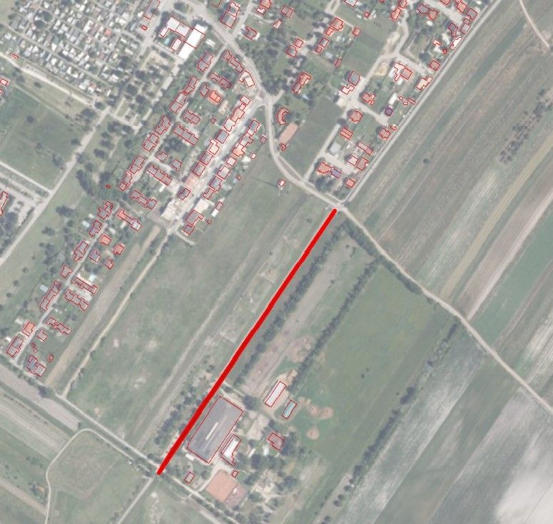 Die Luftaufnahme zeigt eine Stadt mit vielen Gebäuden, von denen die meisten rote Dächer haben. Eine rote Linie durchquert das Bild diagonal.