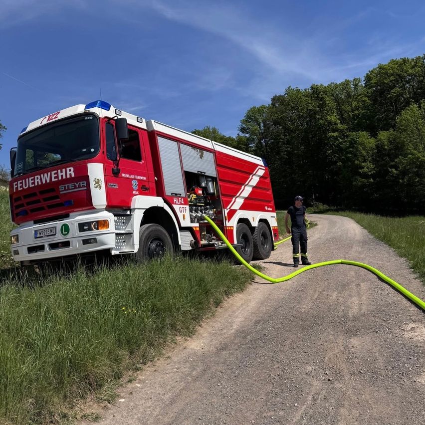 Ein roter Feuerwehrwagen der Feuerwehr Steyr steht am Straßenrand eines unbefestigten Weges.