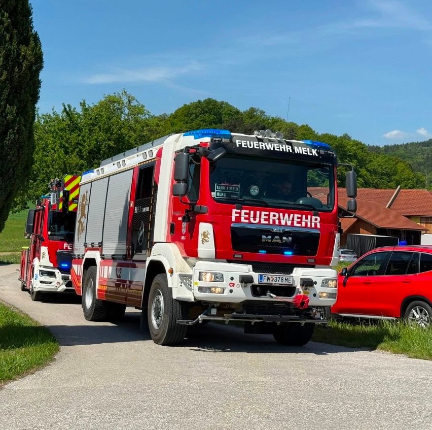 Ein roter Feuerwehrwagen der Feuerwehr Melk fährt eine Straße hinunter. Ein weiterer Feuerwehrwagen folgt.
