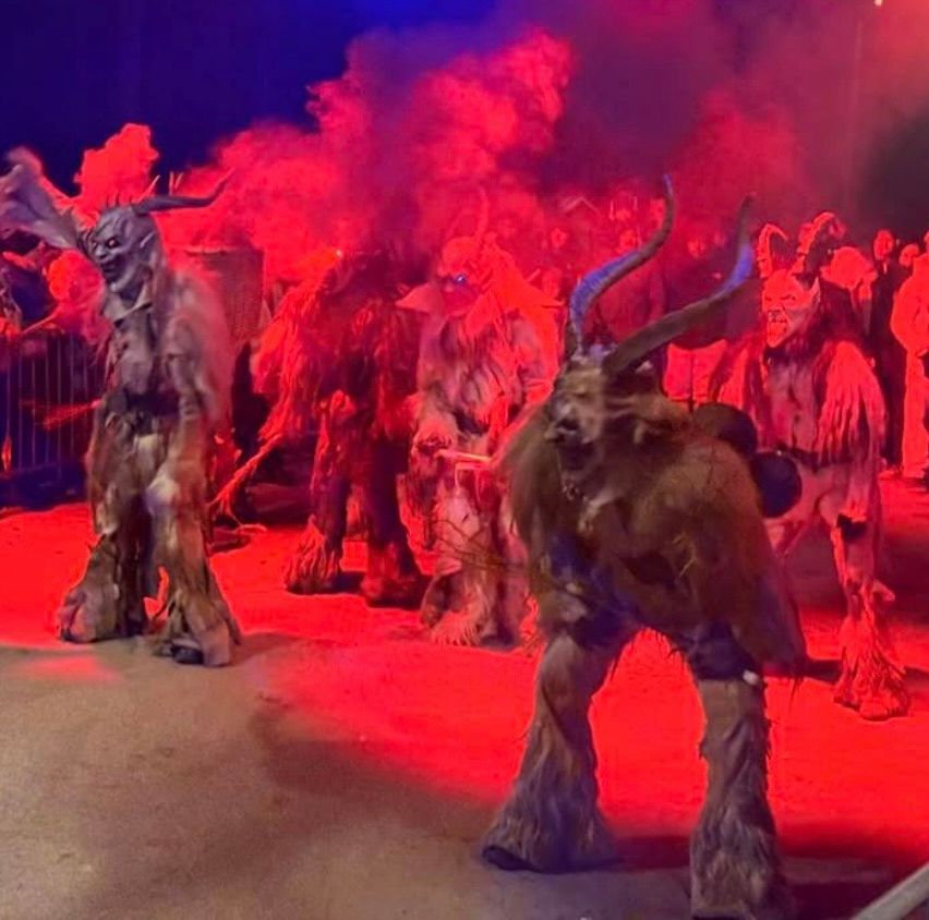 Eine Gruppe von Menschen in Hörnerkostümen und Fellen tritt auf einer Bühne mit rotem Licht und Rauch auf.