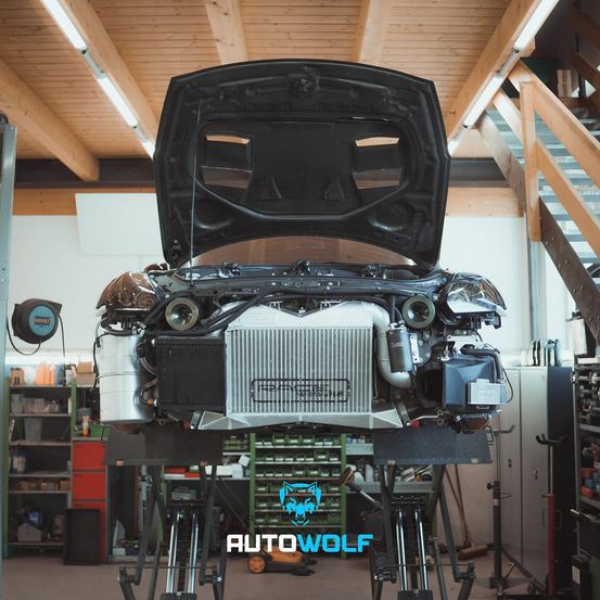 Ein Auto mit geöffneter Motorhaube in einer Werkstatt. Ein Kühler und andere Motorteile sind sichtbar.