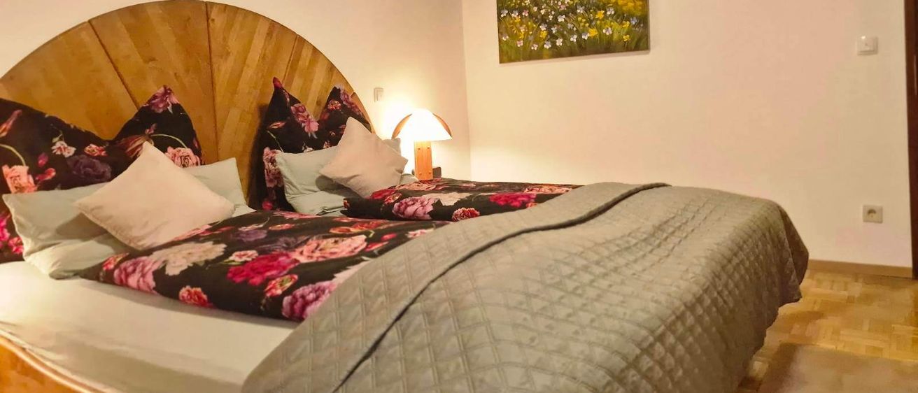 Ein Schlafzimmer mit einem Bett, Kissen und einer Nachttischlampe. Ein Blumengemälde schmückt die Wand.