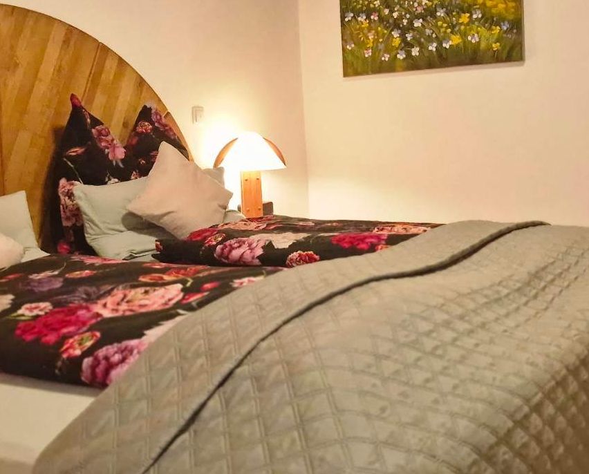 Ein Schlafzimmer mit einem Bett, Kissen und einer Nachttischlampe. Ein Blumengemälde schmückt die Wand.