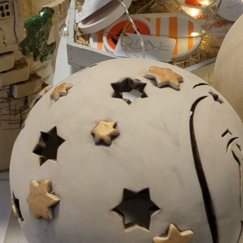 Ein kugelförmiges Keramikobjekt mit Sternenausschnitten und goldenen Sternendekorationen ist auf einem Tisch ausgestellt.