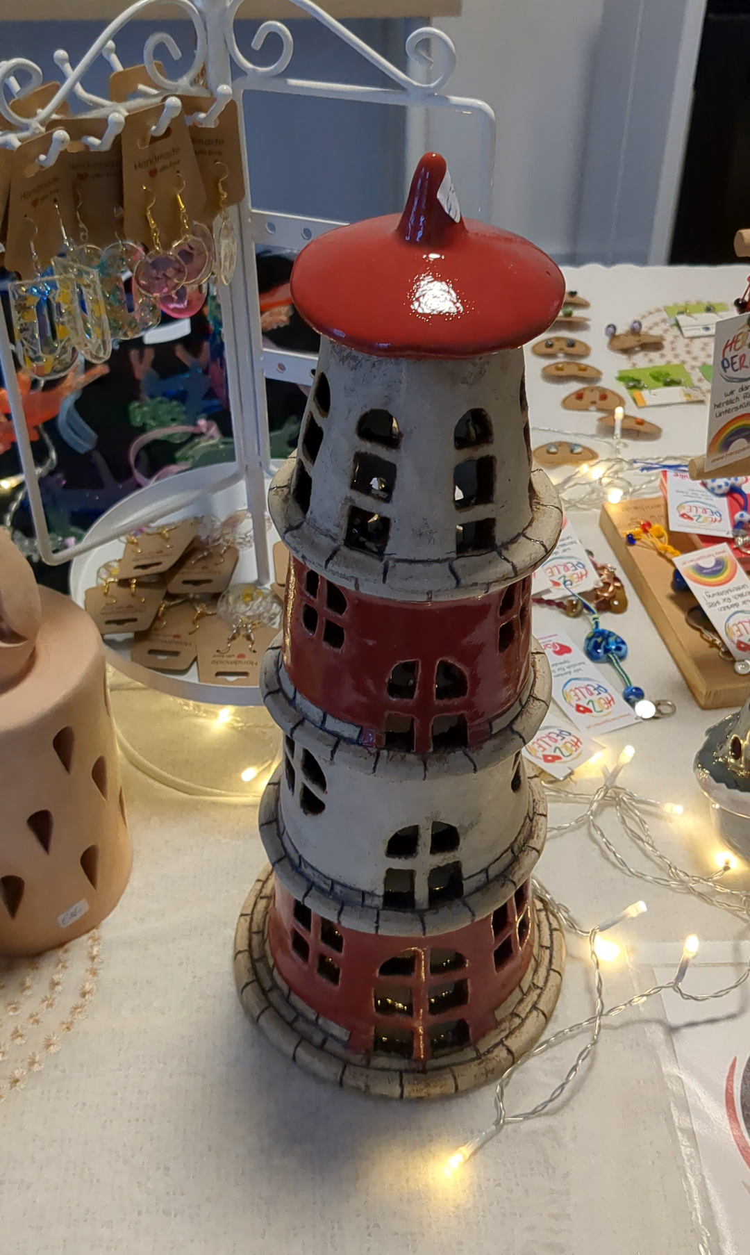 Eine mehrschichtige rote und weiße Keramikstruktur mit rotem Oberteil und mehreren Fenstern, auf einem Tisch mit dekorativen Lichtern und anderen Gegenständen.