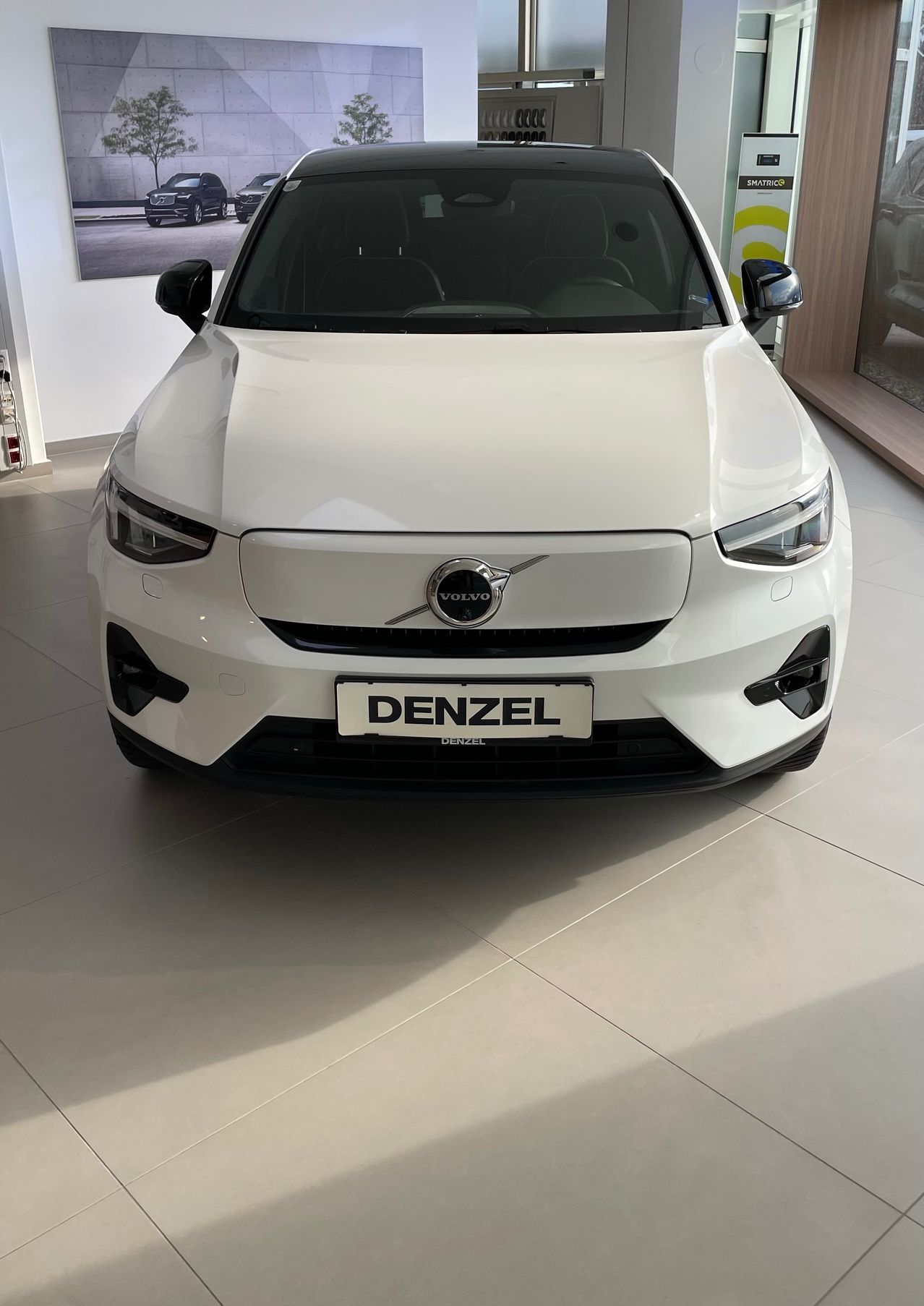 Die Vorderansicht eines weißen Volvo-Autos mit dem Kennzeichen Denzel, das in einer Ausstellungshalle geparkt ist.