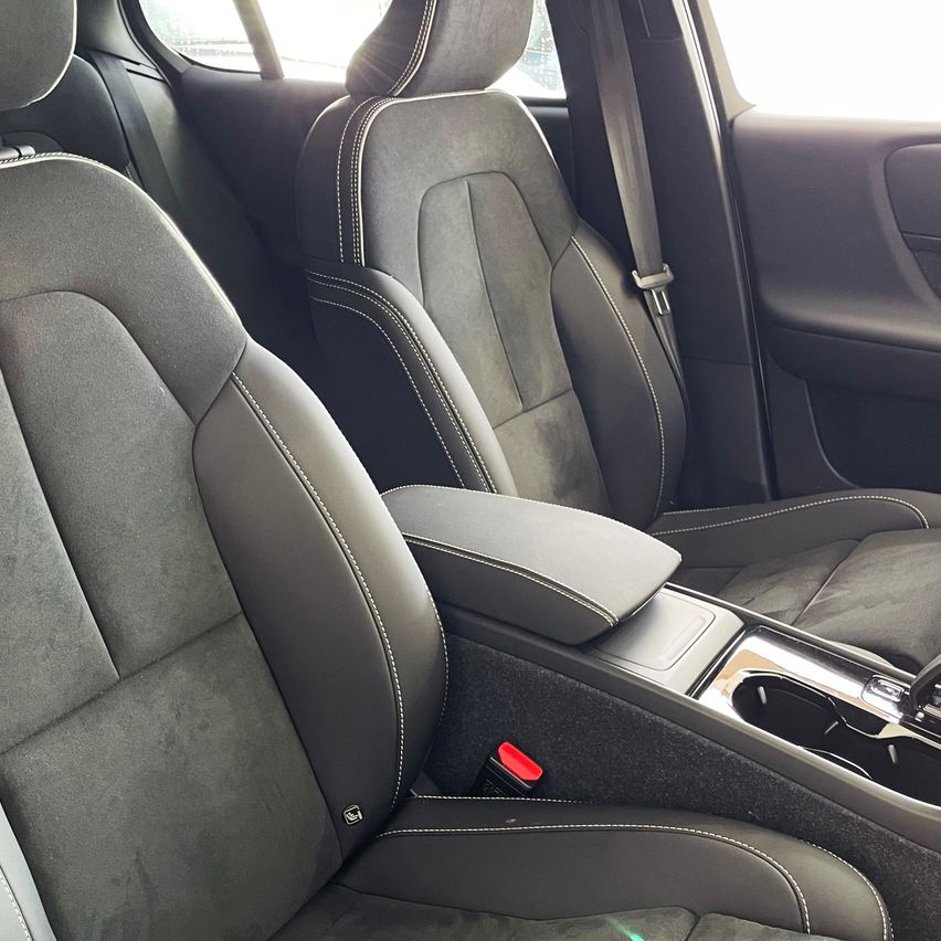 Innenraum eines Autos mit zwei grauen Ledersitzen, einem mit Armlehne und Aschenbecher und dem anderen mit angeschnalltem Sicherheitsgurt.