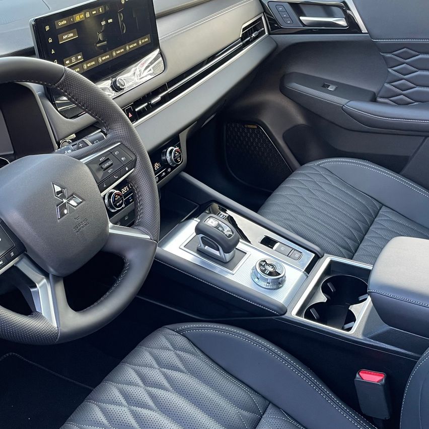 Innenraum eines Mitsubishi Eclipse Cross. Das Armaturenbrett hat ein Touchscreen-Display, Klimasteuerungen und verschiedene Knöpfe. Das Lenkrad ist mit Leder umwickelt.