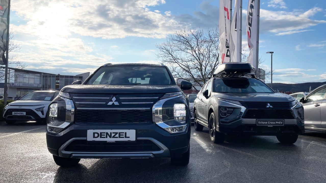 Zwei schwarze Mitsubishi Outlander stehen nebeneinander geparkt vor einem Hintergrund mit bewölktem Himmel.