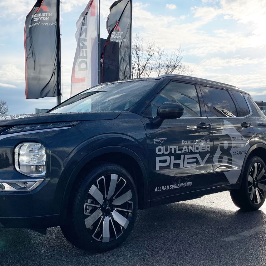 Ein blauer SUV mit Leichtmetallrädern ist vor einem Hintergrund mit Fahnen geparkt.