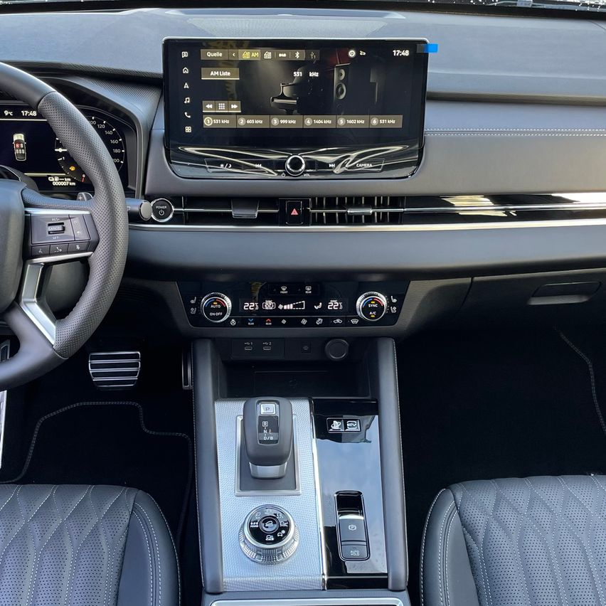 Auto-Armaturenbrett mit Lenkrad und zentralem Display, das Musikplayer und andere Bedienelemente zeigt, beleuchtet durch Umgebungslicht.