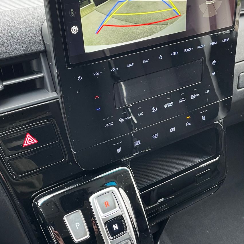 Nahaufnahme eines Auto-Armaturenbretts mit einem Navigationsbildschirm, der eine Kameraansicht, Audiosteuerungen und Gangwahltasten zeigt.