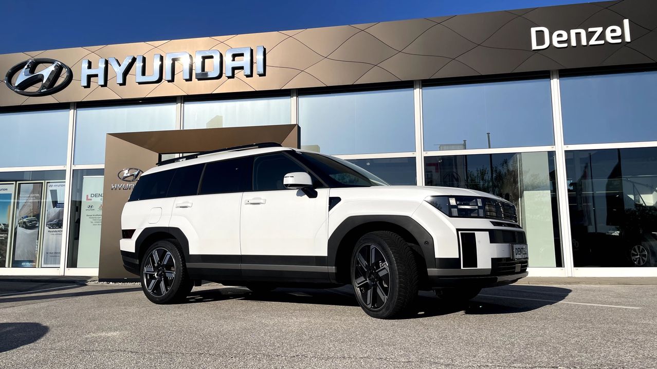 Ein weißer Hyundai SUV steht vor einem Hyundai-Händler unter einem klaren blauen Himmel.