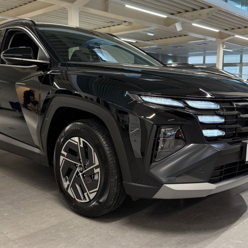 Ein schicker, schwarzer SUV mit silbernen Felgen und Scheinwerfern wird in einer Ausstellungshalle mit gefliestem Boden präsentiert.