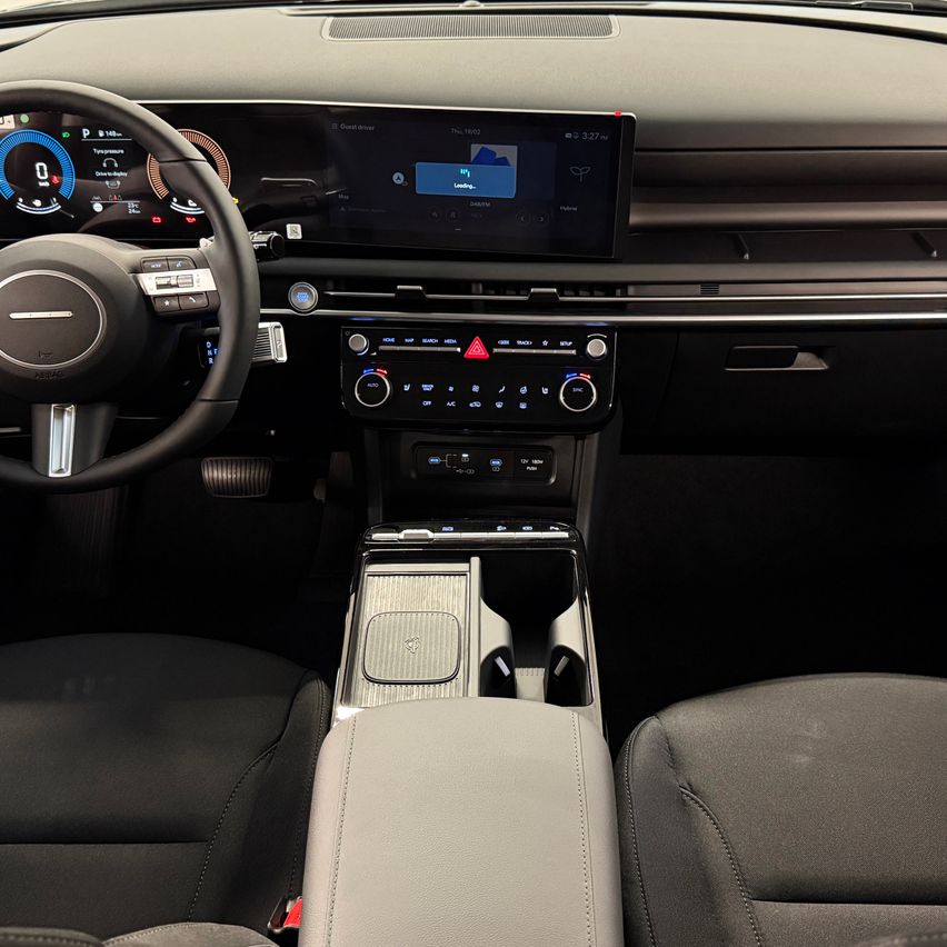 Innenraum eines modernen Autos mit einem Armaturenbrett mit digitalem Display und Lenkrad. Die Mittelkonsole hat Klimasteuerung und ein Touchscreen-Infotainmentsystem. Zwei Ledersitze mit einer Mittelkonsole dazwischen.