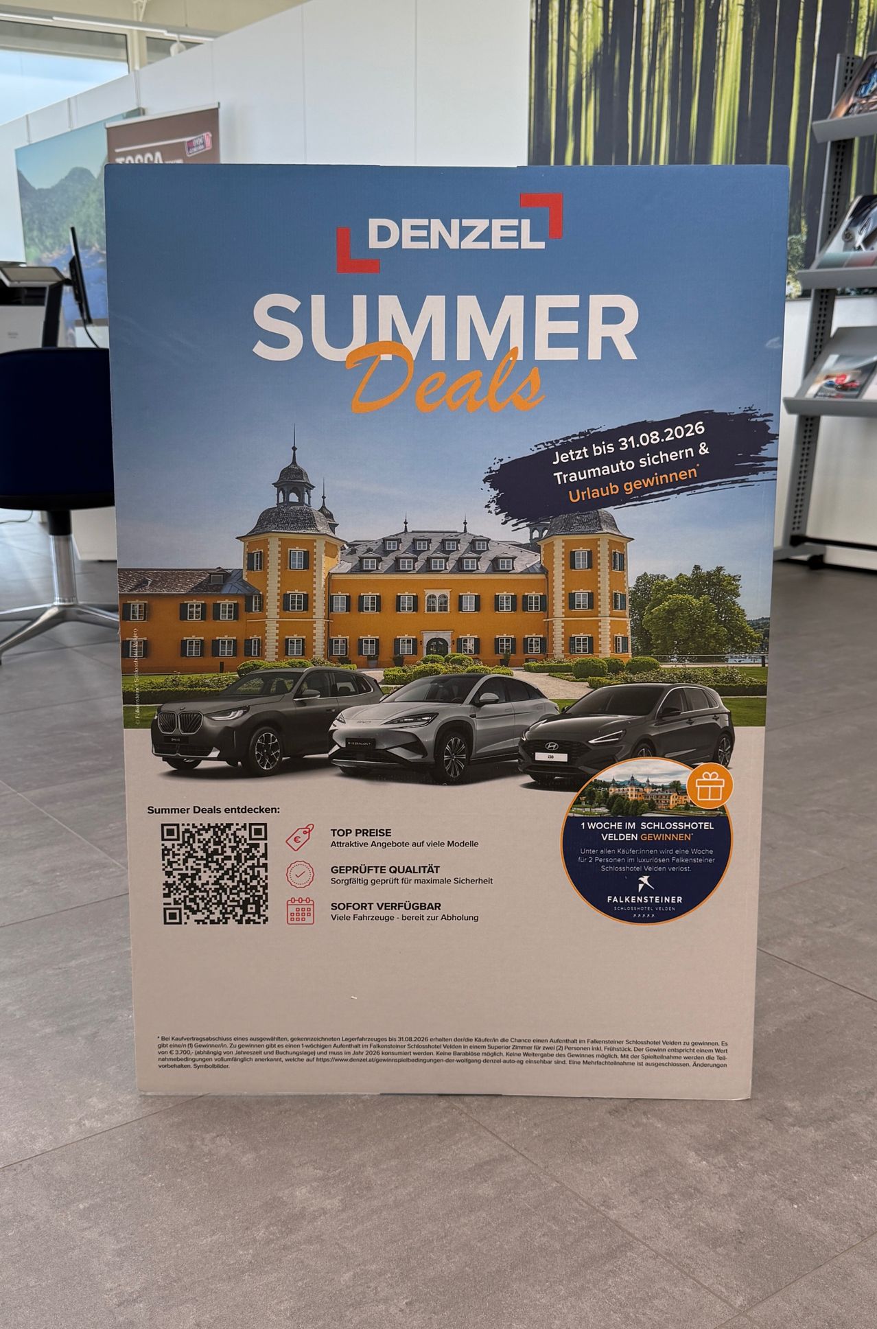 Ein Werbeplakat für Denzel Summer Deals zeigt drei Autos vor einem Schloss mit einem QR-Code, das Top-Preise, Qualitätsgarantien und sofortige Verfügbarkeit anbietet. Das Plakat beinhaltet einen Wettbewerb, um eine Woche im Schlosshotel zu gewinnen.