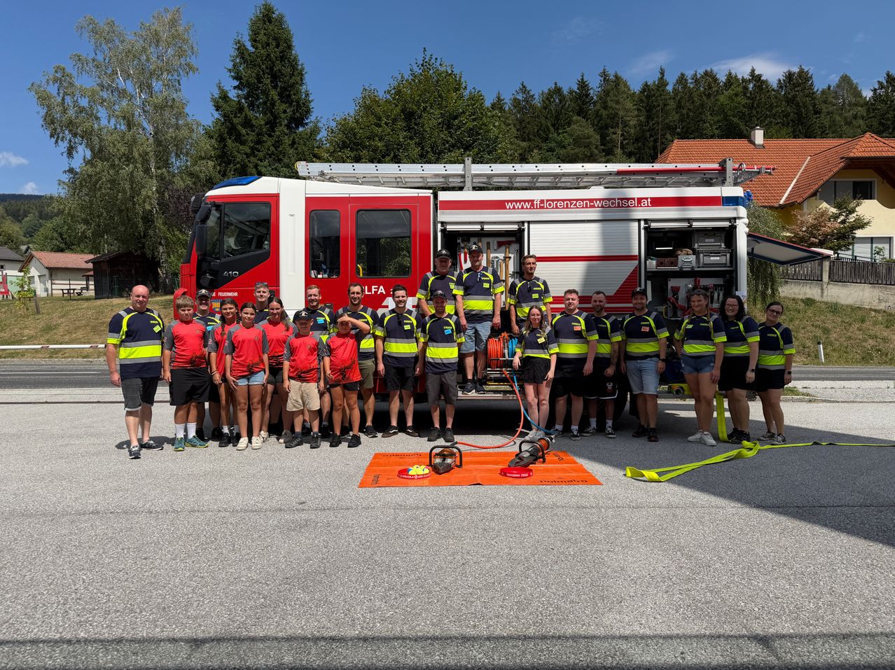A group of firefighters in uniform pose for a photo in front of a fire truck with a website address on its side.
