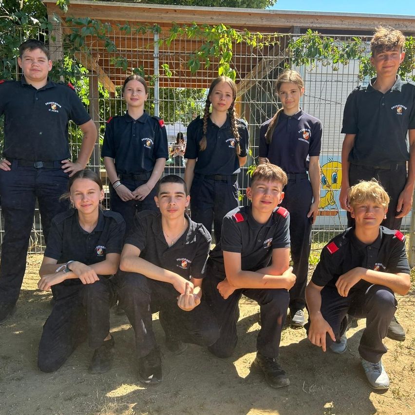 A group of young people in uniforms stand and crouch in front of a metal fence with greenery.