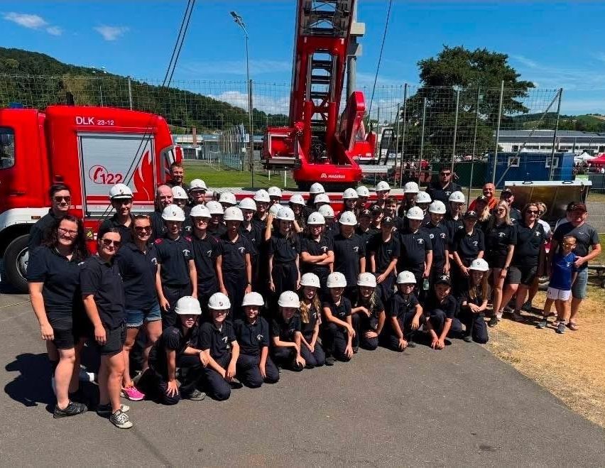 A group of people in firefighting uniforms poses in front of a red fire truck with the number 22 and a fire station in the background.