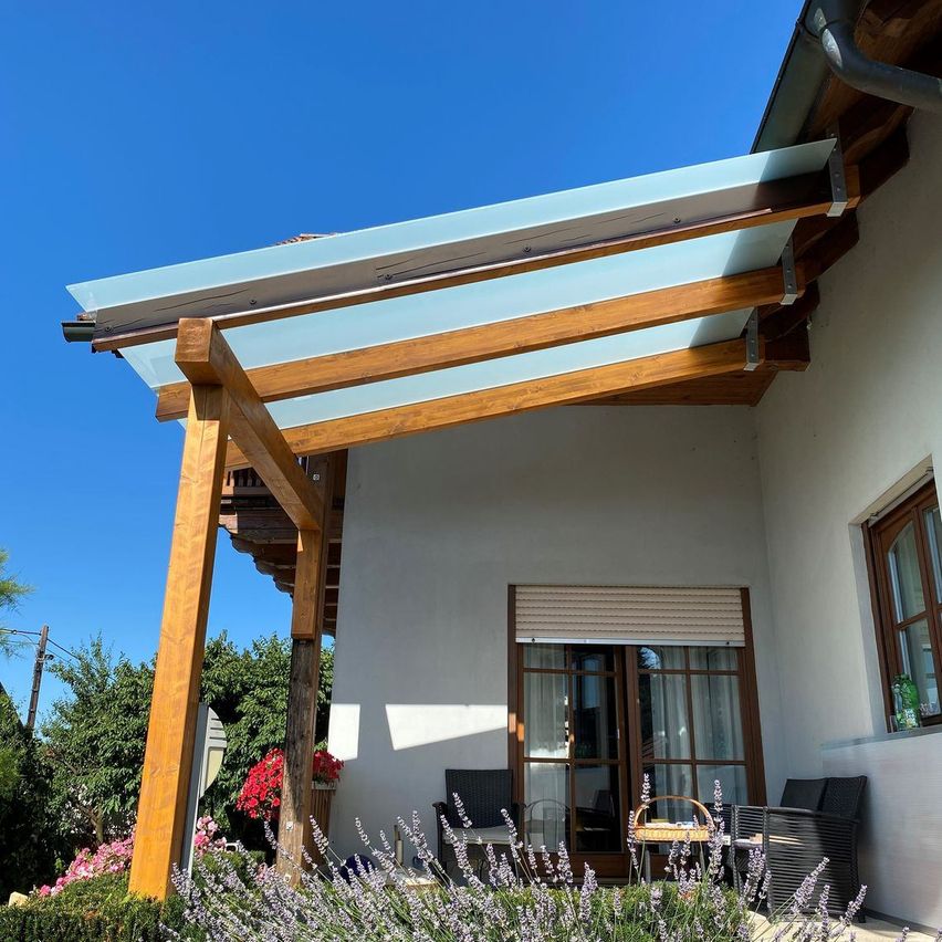 Ein Haus mit einer Veranda und einem Glasdach. Die Veranda hat Holzsäulen und ist von Lavendelpflanzen umgeben.