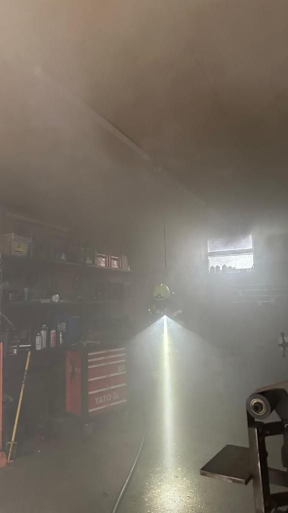 Ein Raum voller Rauch mit einem hellen Licht, Regalen mit verschiedenen Gegenständen, einer roten Werkzeugkiste und einem Fenster.