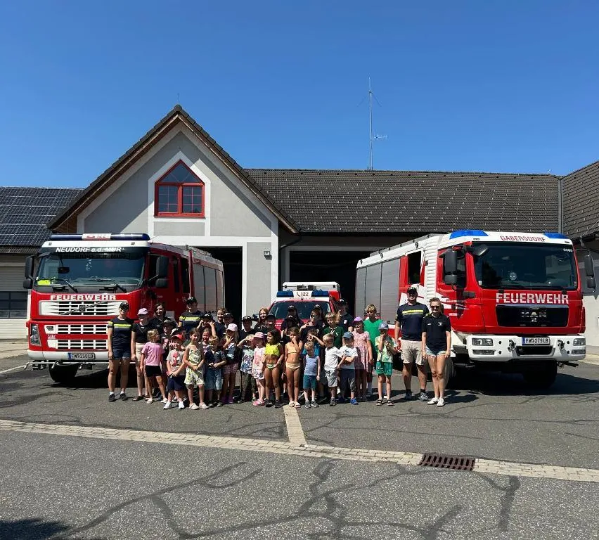 Eine Gruppe von Kindern und Erwachsenen posiert für ein Foto vor zwei Feuerwehrautos und einer Feuerwache.