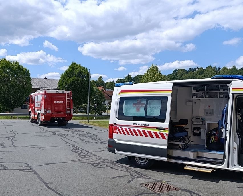Two emergency vehicles are parked on the side of the road under a cloudy sky. The red vehicle has a ladder and the white vehicle has an open door.