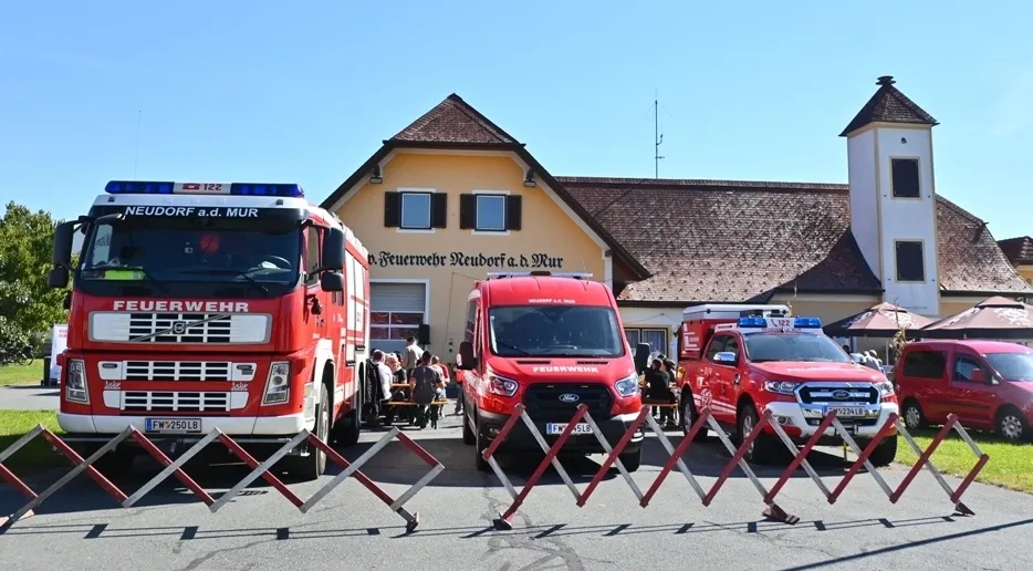 Eine Gruppe von Rettungsfahrzeugen, einschließlich Feuerwehrwagen und Krankenwagen, steht vor einem Gebäude mit dem Schriftzug 'Feuerwehr Neudorf a.d. Mur'.