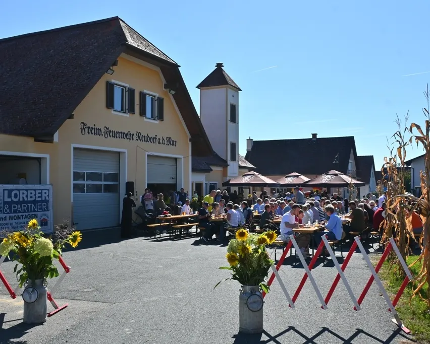 Eine Gruppe von Menschen sitzt an Tischen vor einem Gebäude mit einem Schild, auf dem Lorber & Partner steht.