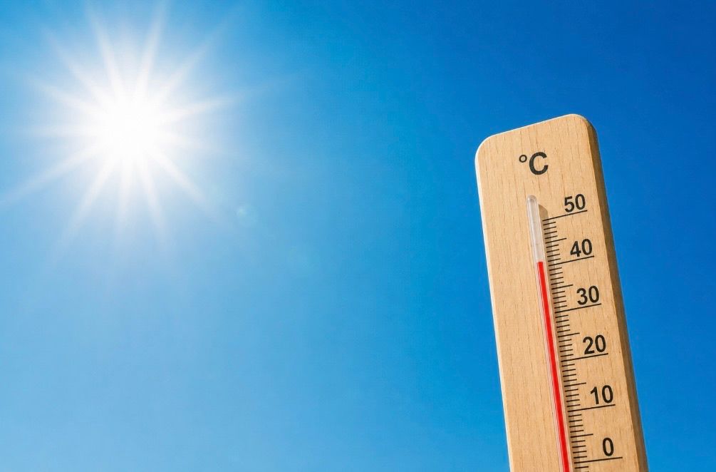 Ein Thermometer mit einer roten Flüssigkeitssäule, die eine Temperatur von 30 Grad Celsius anzeigt, vor einem hellblauen Himmel mit strahlend heller Sonne.