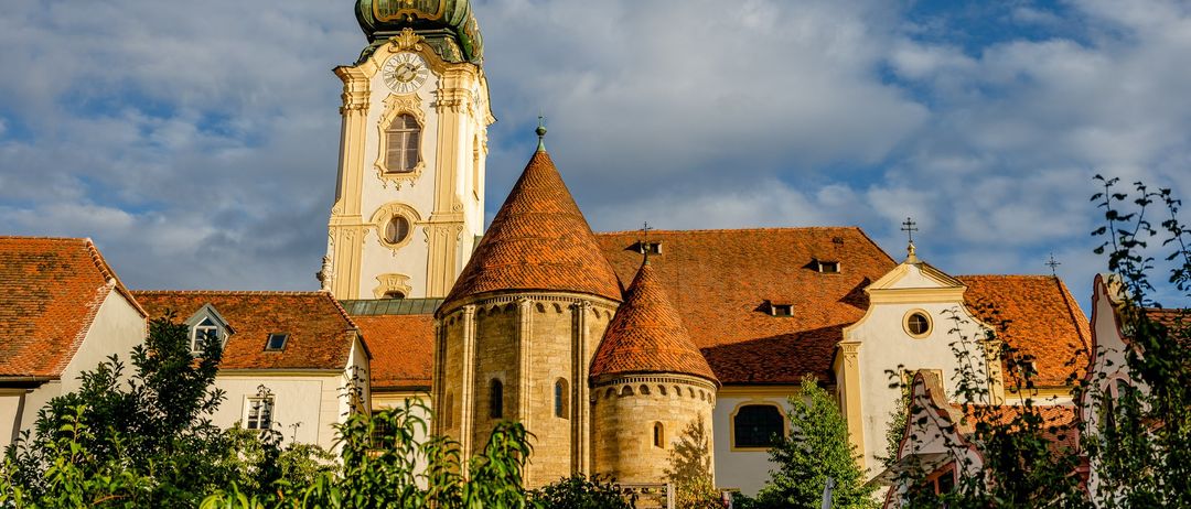 Eine gotische Kirche mit einem hohen Turm und rotem Dach, umgeben von Grün unter einem teilweise bewölkten Himmel.