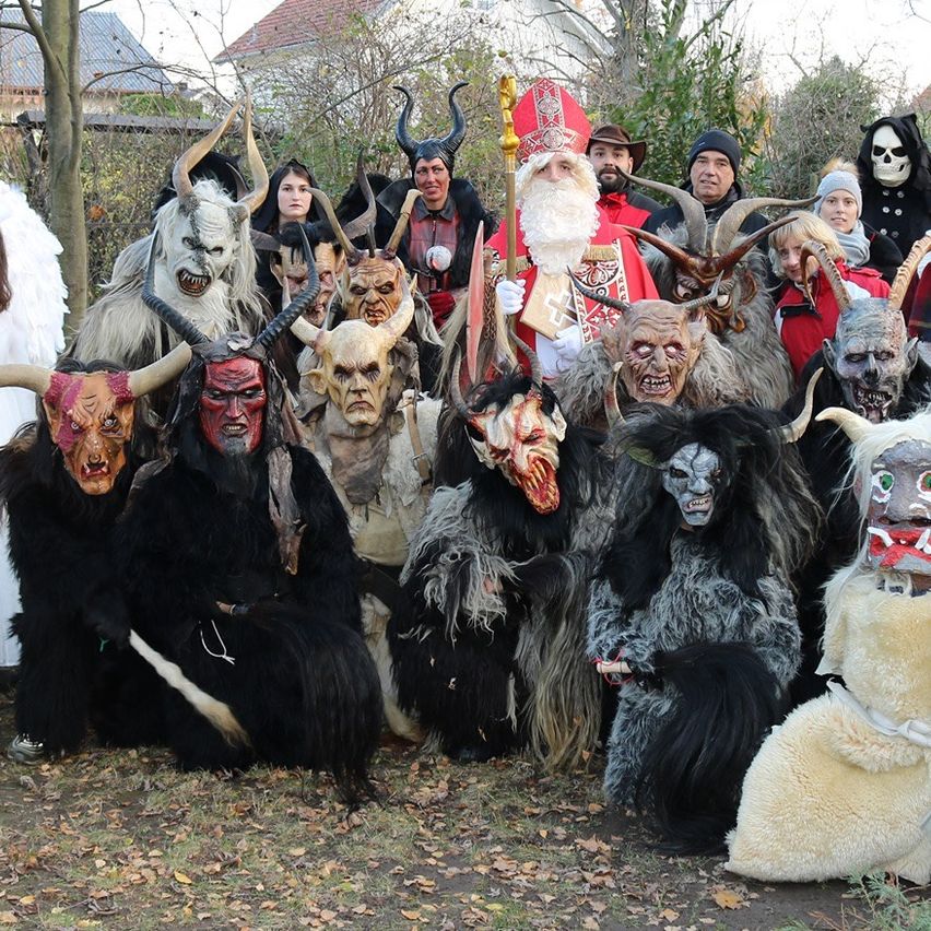Eine Gruppe von Menschen in verschiedenen Kostümen, einschließlich Engel, Teufel und Weihnachtsmann, posiert für ein Foto im Garten.