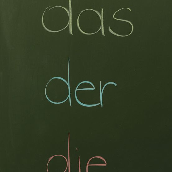 Eine Kreidetafel mit den deutschen Wörtern 'das der die' in verschiedenen Farben. 'Das' in weiß, 'der' in blau und 'die' in rot.