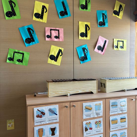Ein Holzschrank enthält zwei Xylophon oben. Die Wand hat Musiknoten und Instrumente darauf. Der Schrank hat Musiknotenkarten darauf.