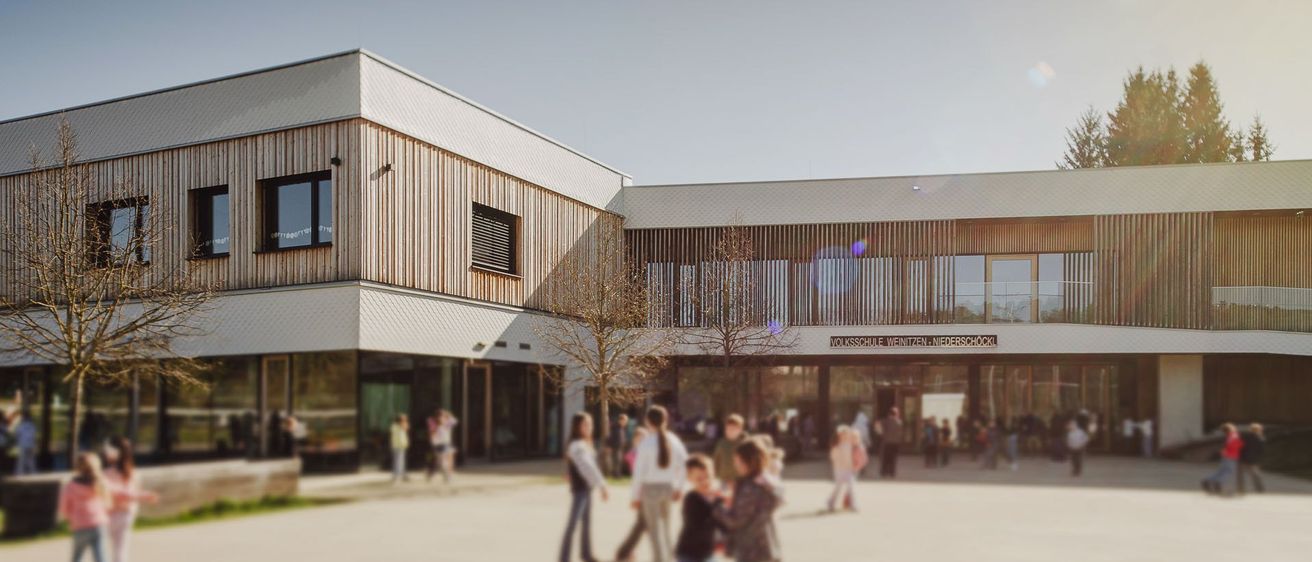 Schüler und Mitarbeiter versammeln sich vor einem modernen Schulgebäude mit Glasfenstern und hölzernen Fassaden unter klarem Himmel.