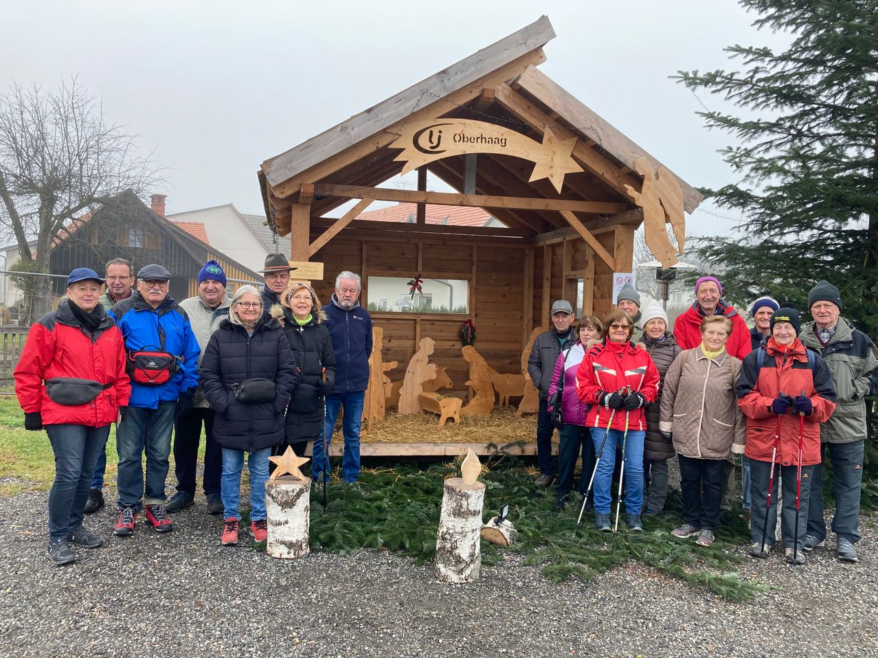 Eine Gruppe von Menschen posiert vor einer Krippe, wahrscheinlich bei einer Feierlichkeit. Die Holzstruktur trägt ein Schild mit der Aufschrift 'Oberhaag'.