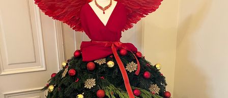 Ein rotes Engelkostüm wird auf einem Mannequin ausgestellt. Das Kostüm hat Flügel und eine Halskette und ist mit einem Weihnachtsbaumrock dekoriert.
