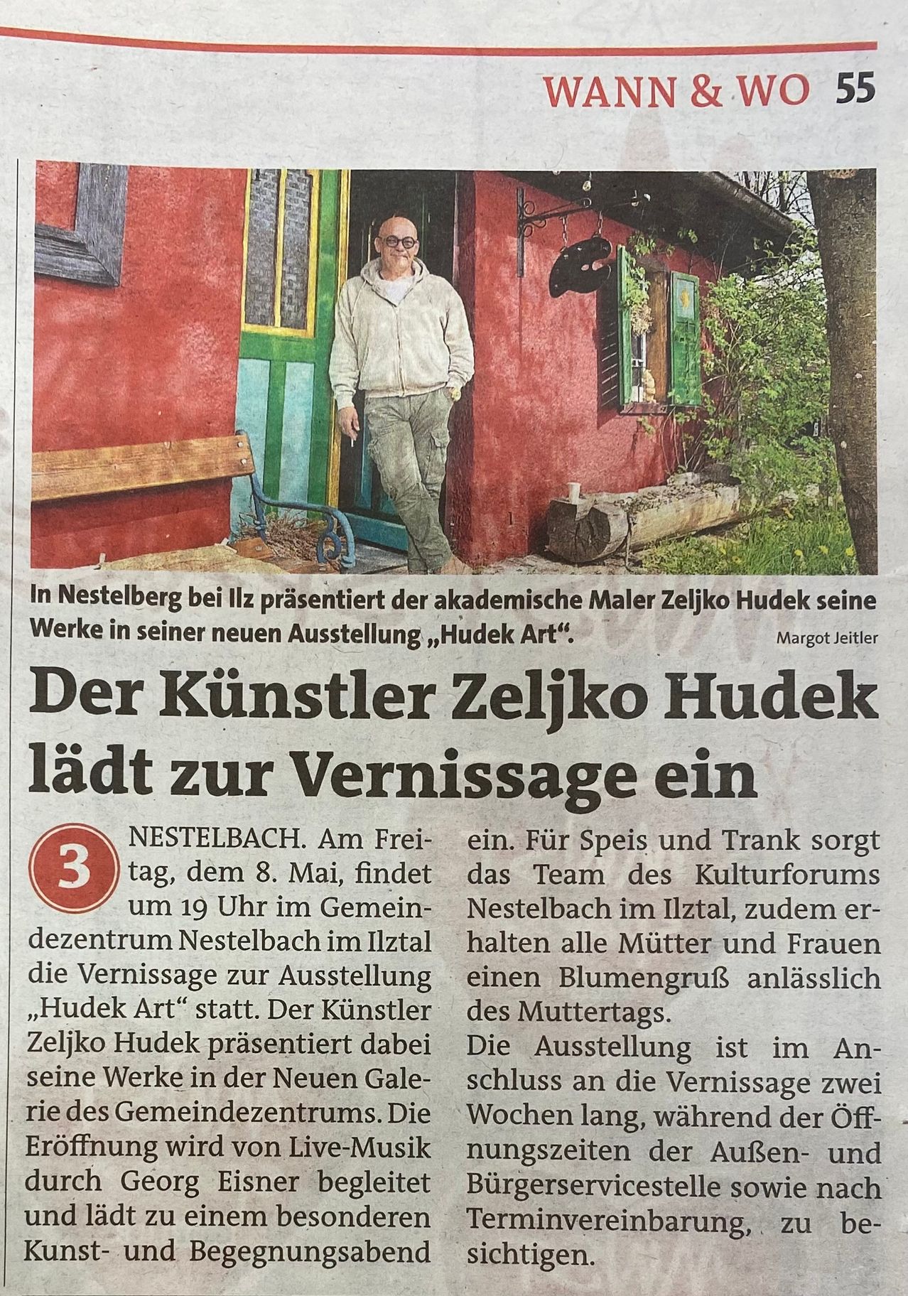 Ein Zeitungsartikel zeigt den akademischen Maler Zeljko Hudek, der seine neue Ausstellung 'Hudek Art' in Nestelberg präsentiert. Der Künstler steht vor einem roten Haus mit einer Bank und Pflanzen. Die Ausstellung findet am 8. Mai statt.
