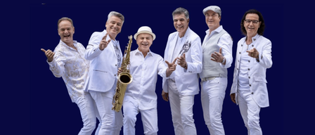 Eine Gruppe älterer Männer in weißen Kleidern posiert für ein Foto. Einer hält eine Saxophon.