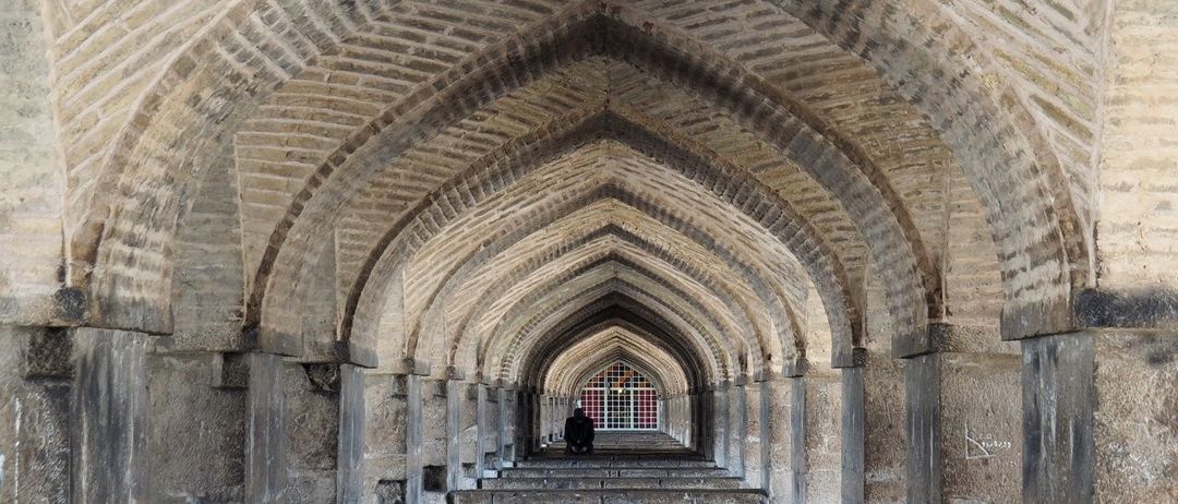 Das Innere einer alten architektonischen Struktur mit gewölbter Steindecke und -wänden, mit einer Person, die auf den Stufen sitzt.