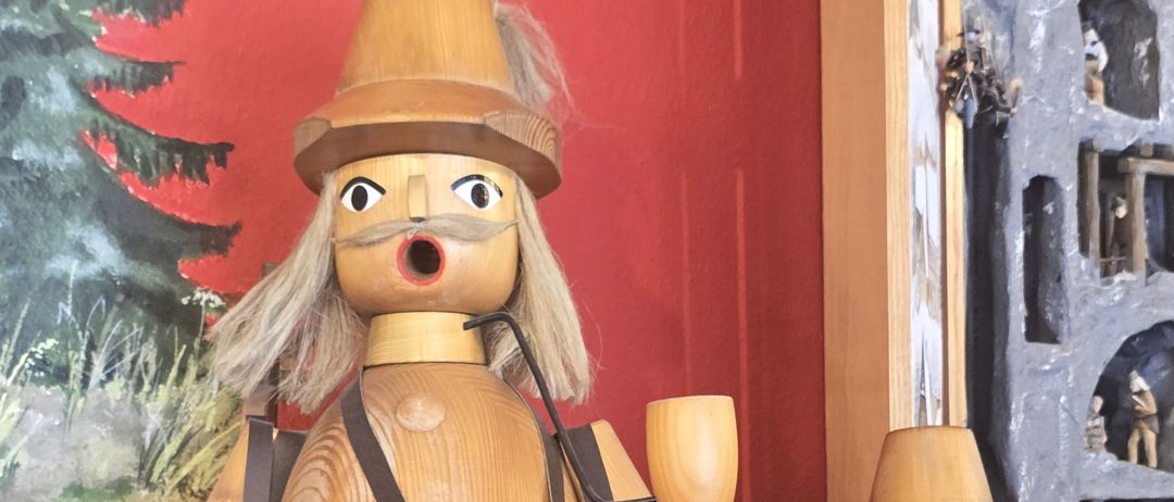 Zwei hölzerne Waldhüter-Figuren mit Ferngläsern und Stöcken stehen vor einer roten Wand. Eine hat ein hölzerne Horn und die andere hat einen Stock.