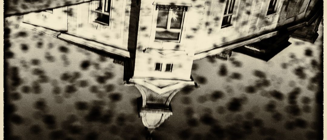 Ein Schwarz-Weiß-Bild der Reflexion eines Gebäudes im Wasser, mit sichtbaren Fenstern und einem spitzen Dach.