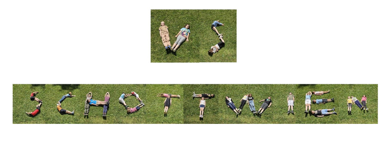 Kinder, die auf dem Gras liegen, bilden mit ihren Körpern die Buchstaben des Wortes SPIEL.
