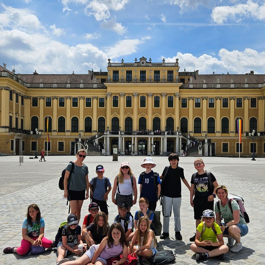 Eine Gruppe von Kindern und ihren Lehrern posiert für ein Foto vor dem Schloss Schönbrunn.