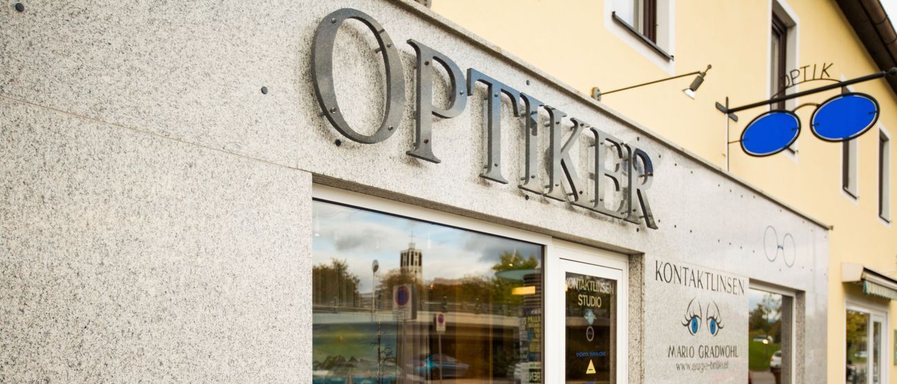 Das Schaufenster eines Optikers namens Optiker, mit einer Glastür, einer Ausstellung von Brillen und einem Schild an der Wand.