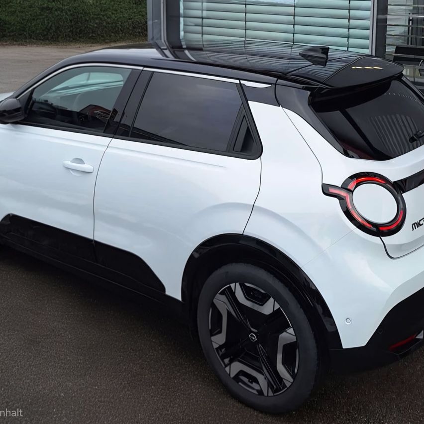 Ein weißer SUV mit schwarzem Dach und Akzenten, geparkt auf einer gepflasterten Oberfläche. Hinten ist ein rotes kreisförmiges Lichtdesign zu sehen.